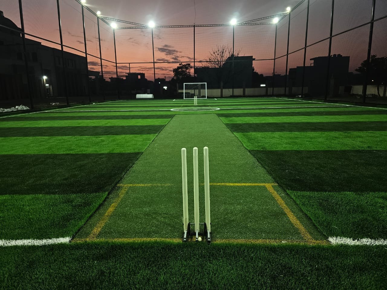 Floodlit cricket turf at dusk with pitch and stumps